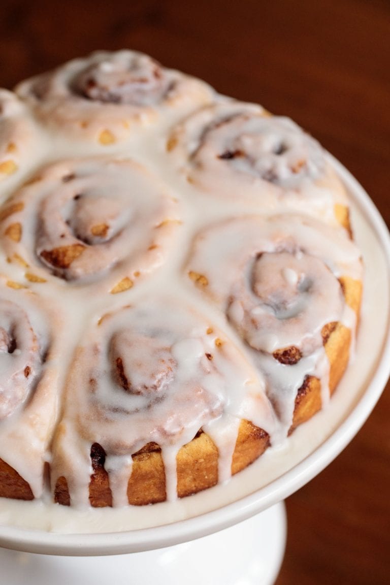 Vertical picture of iced cinnamon rolls on a white cake stand