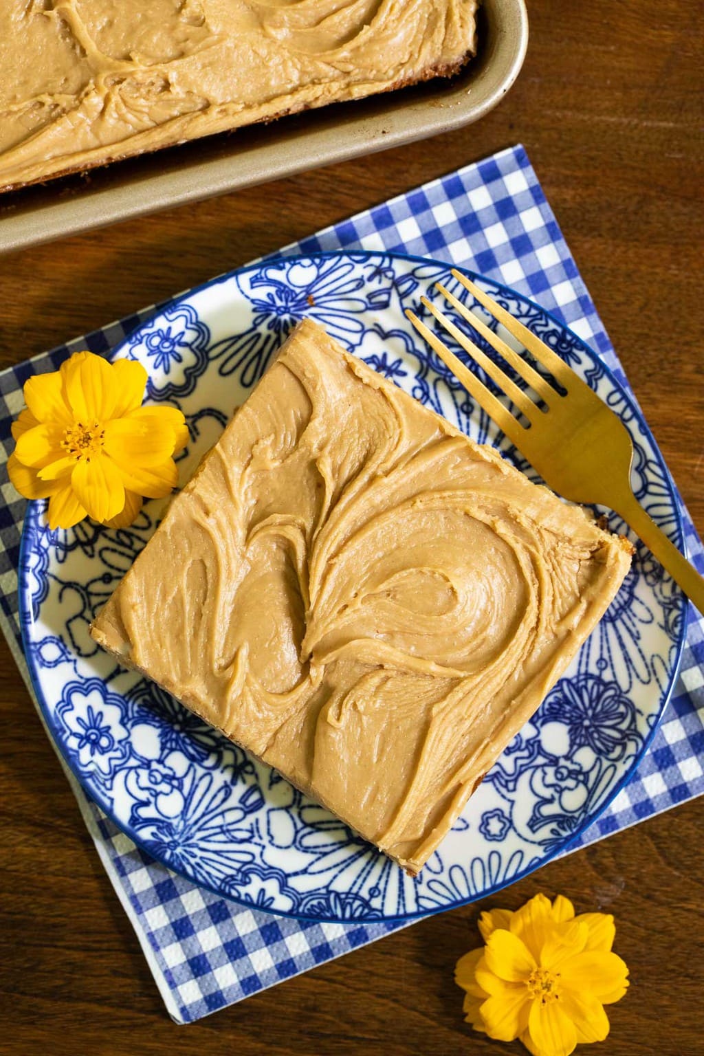 Overhead vertical photo of a piece of Peanut Butter Texas Sheet Cake on a blue and white patterned serving plate.