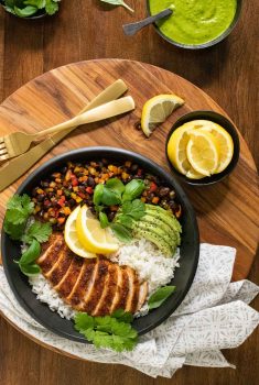 Overhead vertical photo of a Peruvian Chicken Rice Bowl garnished with lemon and avocado wedges and sprigs of fresh cilantro.