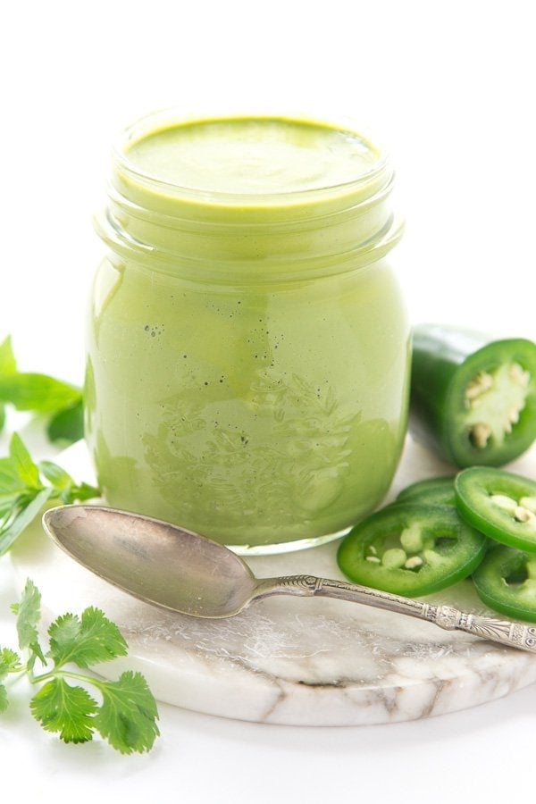 Vertical closeup photo of Peruvian Green Sauce surrounded by fresh cilantro and peppers.
