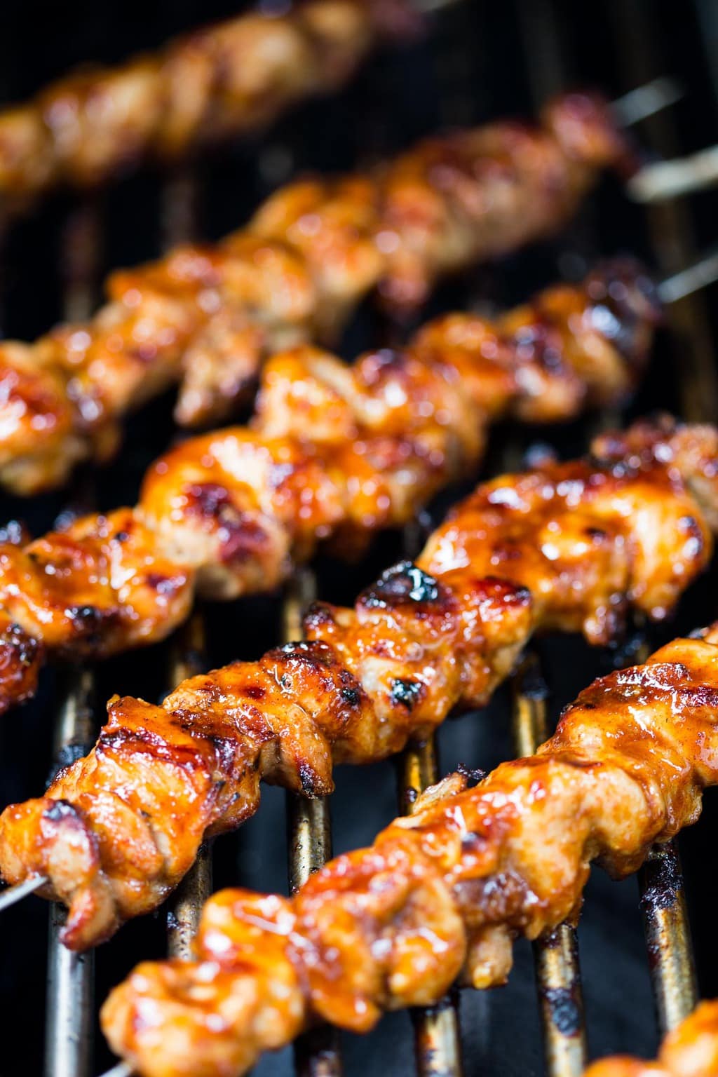 Vertical closeup grille photo of Peruvian Grilled Chicken Skewers being cooked on an outdoor grille.