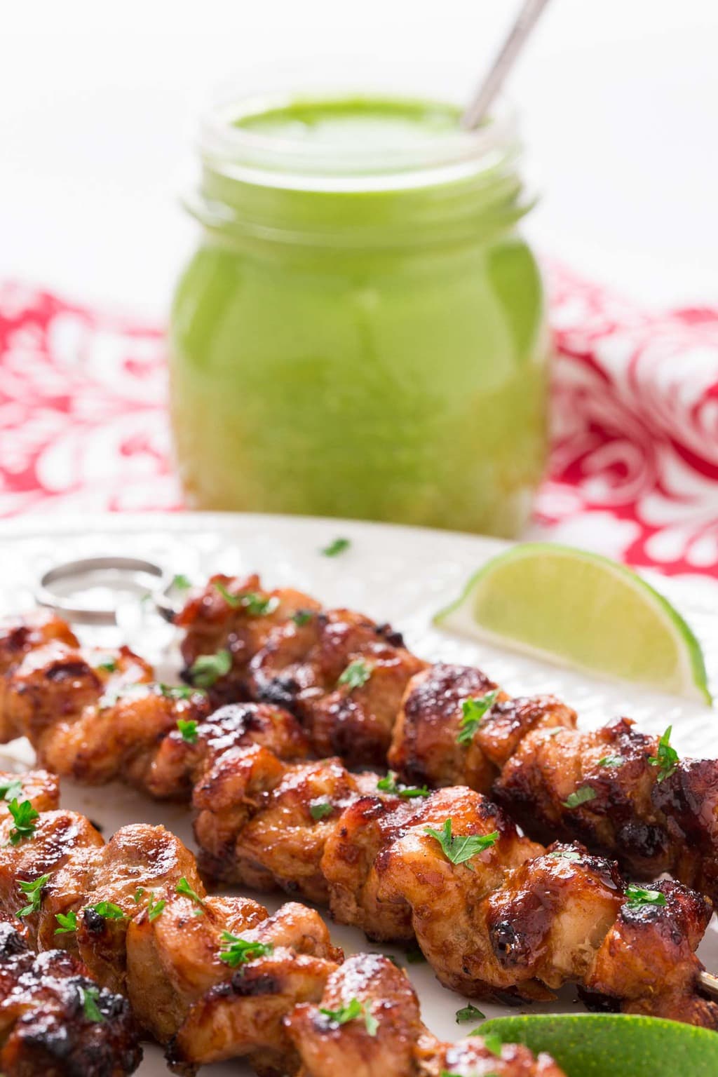 Ultra closeup photo of a serving platter filled with Peruvian Grilled Chicken Skewers with a glass jar filled with Peruvian Green Sauce in the background.