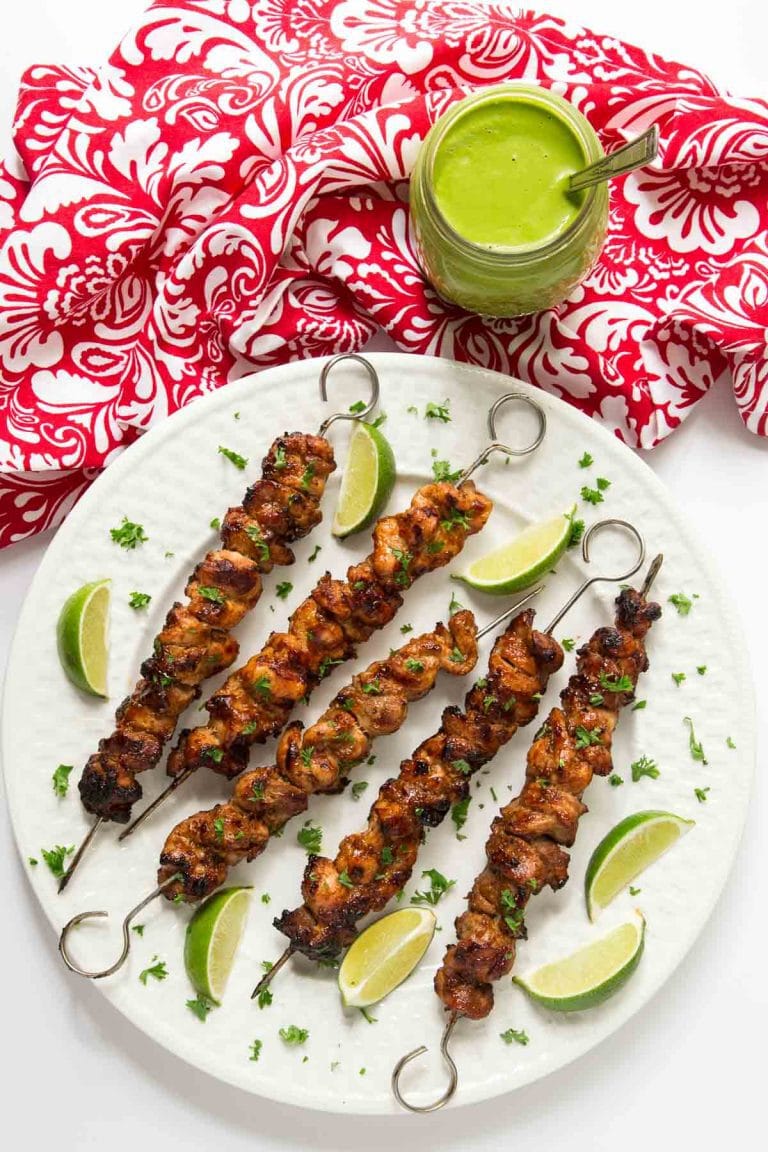 Peruvian Grilled Chicken Skewers on a white plate with a green sauce and red and white napkin.