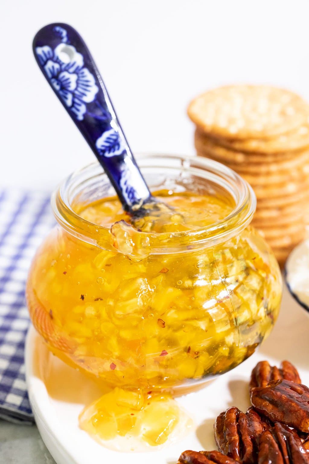 Vertical photo of a Weck glass jar of Pineapple Habanero Pepper Jelly surrounded by appetizer items.