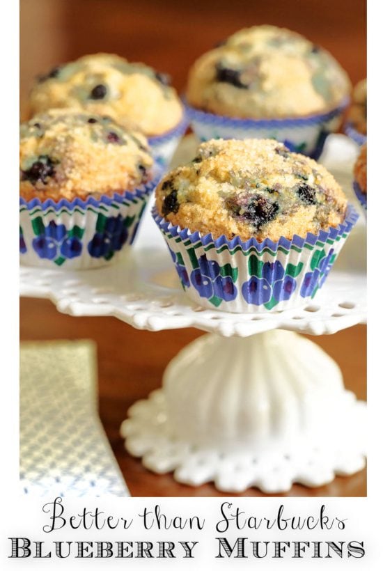 Vertical closeup photo of a batch of Better than Starbucks Blueberry Muffins on a white pedestal serving plate.