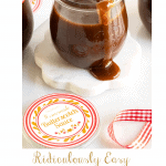 Vertical photo of a jar of Ridiculously Easy Butterscotch Sauce with sauce pouring over the edge of the jar and custom Butterscotch Sauce labels in the foreground.