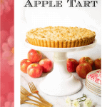 Vertical photo of an Easy French Apple Tart on a white pedestal presentation plate surrounded by apples in the background and a graphic, "Easy French Apple Tart" at the top.