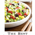 Vertical closeup photo of The BEST Greek Salad in a marble serving bowl on a wood table.