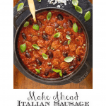 Overhead vertical photo of a Staub pot filled with Italian Sausage Puttanesca on a round grey slate surface garnished with fresh basil leaves.