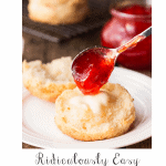 Vertical closeup photo of a Ridiculously Easy Buttermilk Biscuit on a white serving plate with strawberry jam being poured onto it.