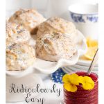 Vertical photo of Ridiculously Easy Lemon Poppy Seed Scones on a white scalloped presentation platter with a small jar of Raspberry Freezer Jam in the foreground.