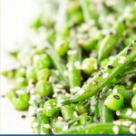 Vertical extreme closeup of Sesame Ginger Green Bean Salad on a white serving plate with a graphic title in blue and white at the bottom of the photo.