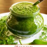Vertical closeup photo of a glass Weck jar filled with Zhoug Sauce, surrounded by fresh cilantro and parsley leaves.