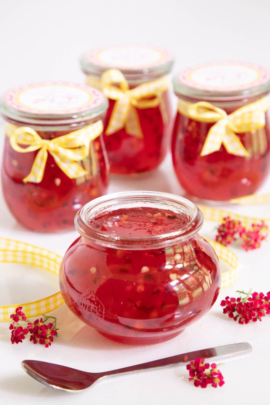 Vertical photo of glass Weck jars of Plum Ginger Pepper Jelly decorated with yellow and white checked ribbons and custom jelly labels.