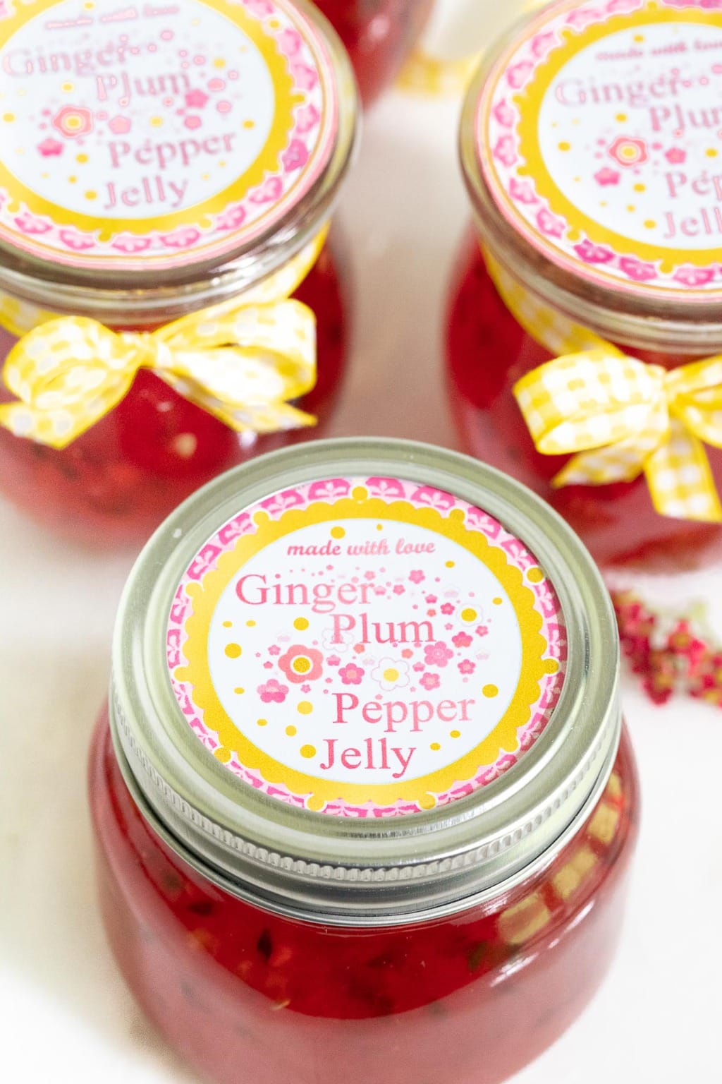 Extreme closeup photo of the top label on jars of Plum Ginger Pepper Jelly decorated with yellow and white checkered ribbons.