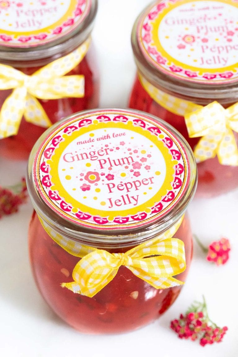 Vertical picture of plum ginger pepper jelly in glass jars with printed labels and yellow ribbons