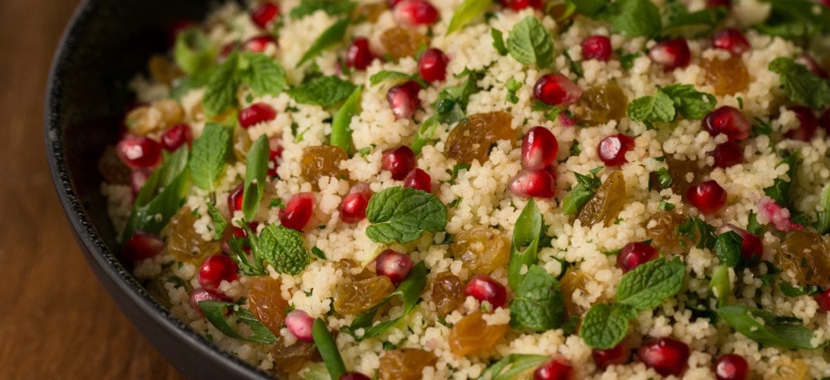 Photo of a bowl of Pomegranate Parsley Couscous Salad on a wood table.