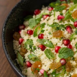 Close up vertical picture of pomegranate parsley couscous salad in a black bowl