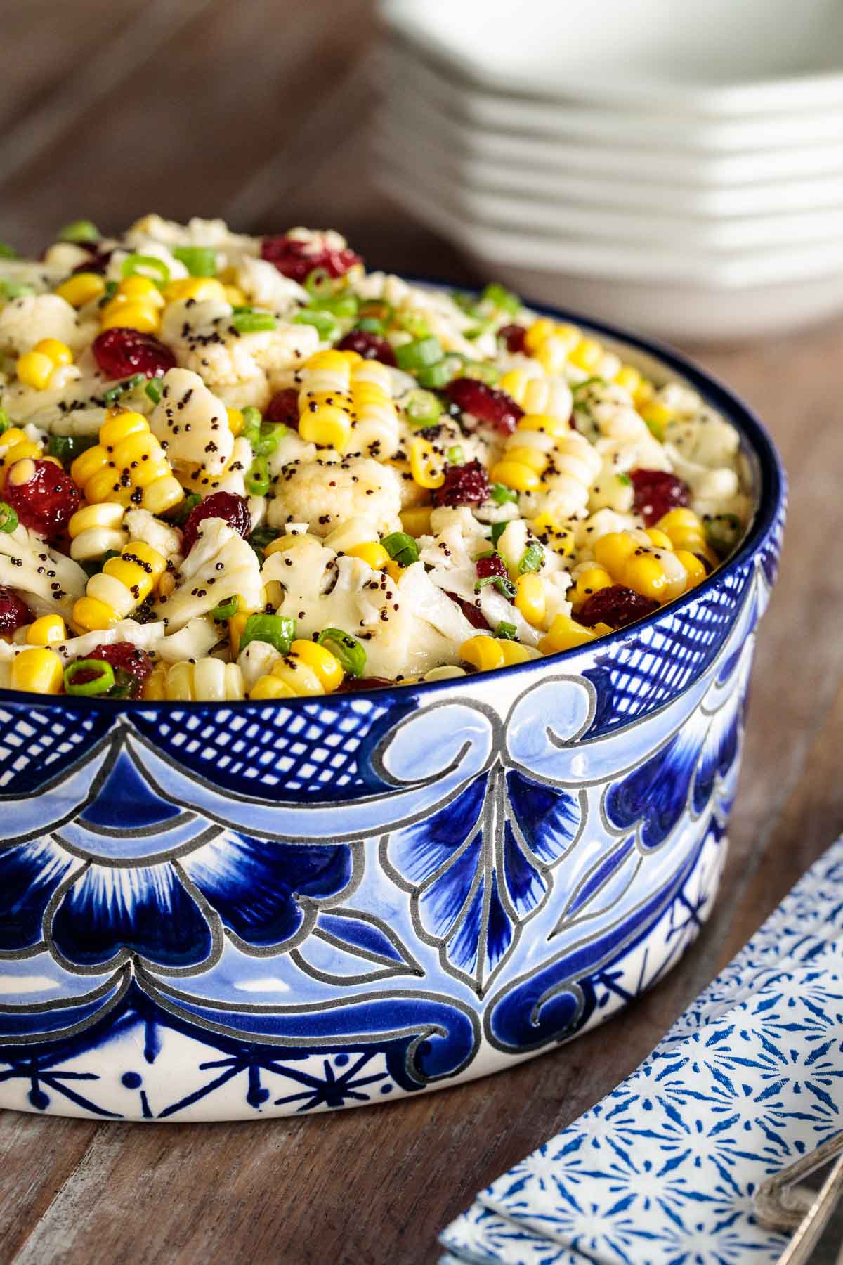 Vertical photo of a Cauliflower and Fresh Corn Salad in a blue and white patterned bowl on a wooden table.
