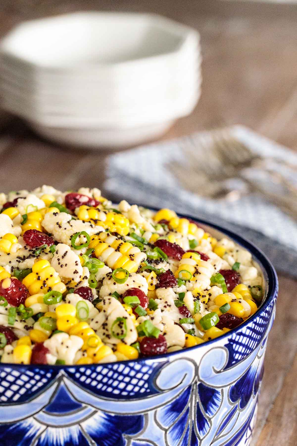 Photo of a serving bowl filled with Poppyseed Cauliflower and Fresh Corn Salad. Serving dishes, utensils and napkins are in the background.
