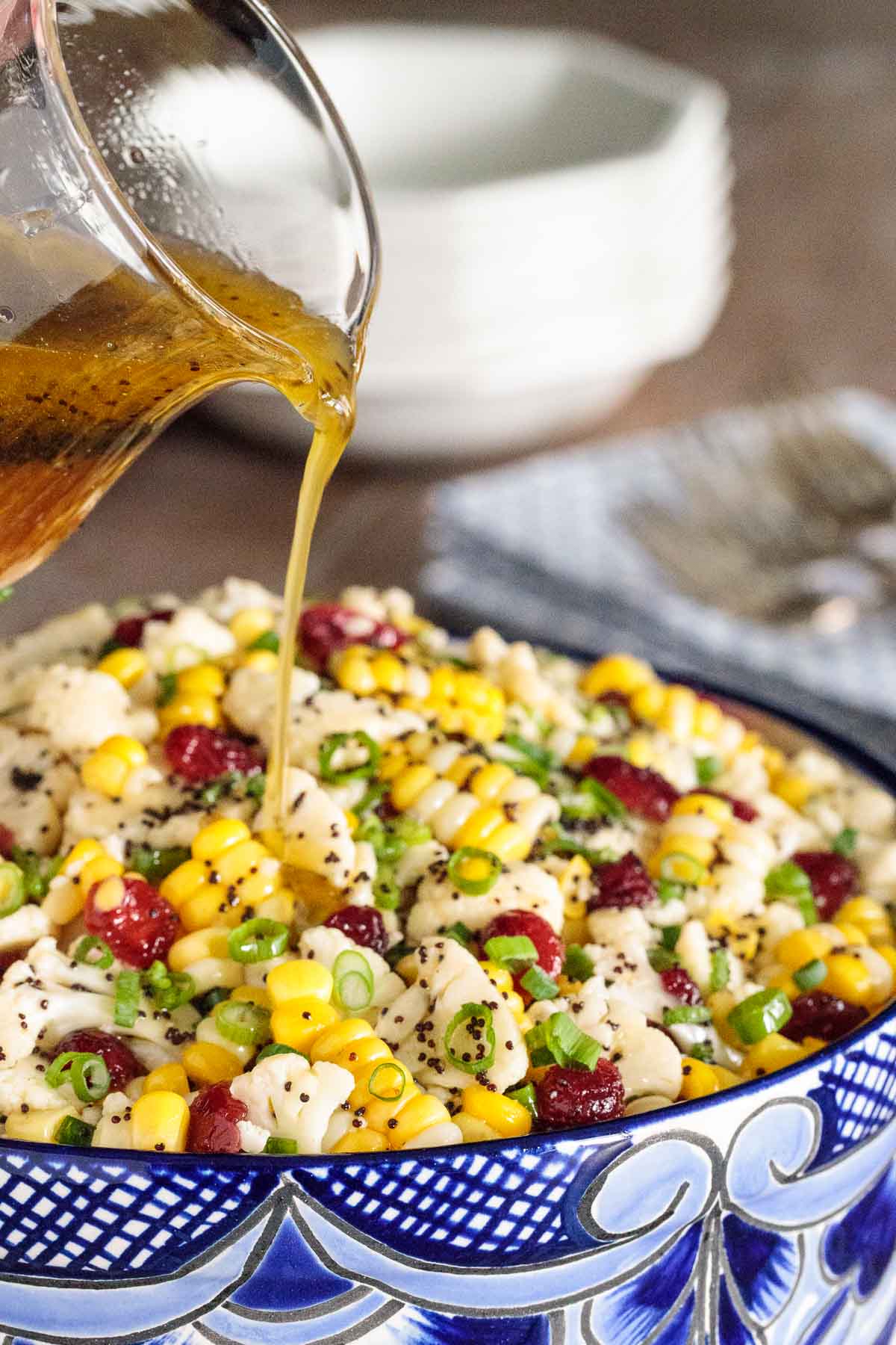Close up photo of a Poppyseed Cauliflower and Fresh Corn Salad with dressing being poured over the salad.