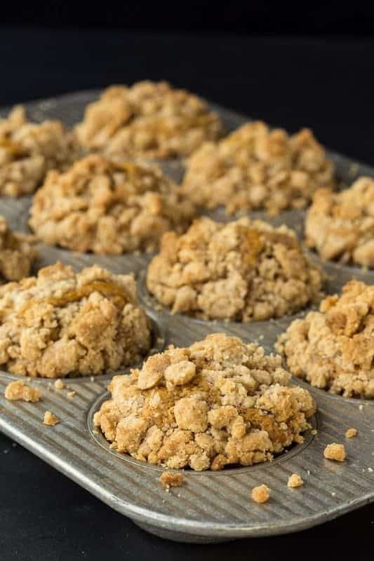 Vertical photo of a muffin pan full of Pumpkin Crumb Muffins against a black background.