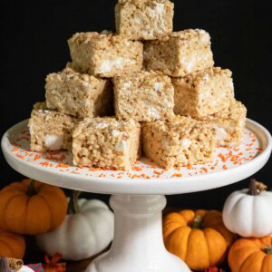 Vertical picture of pumpkin spiced brown butter rice krispie treats on a white cake stand