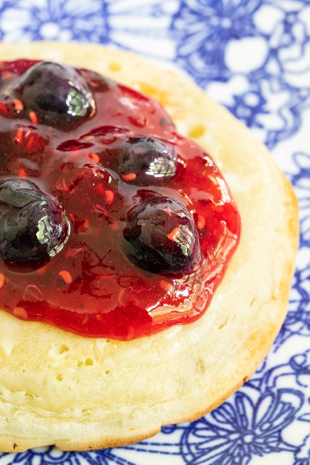 Ultra closeup vertical photo of Queen's Jam (Raspberry Blueberry Jam) on a crumpet.