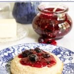 Vertical closeup photo Queen's Jam (Raspberry Blueberry Jam) in a glass canning jar and on a crumpet in the foreground.