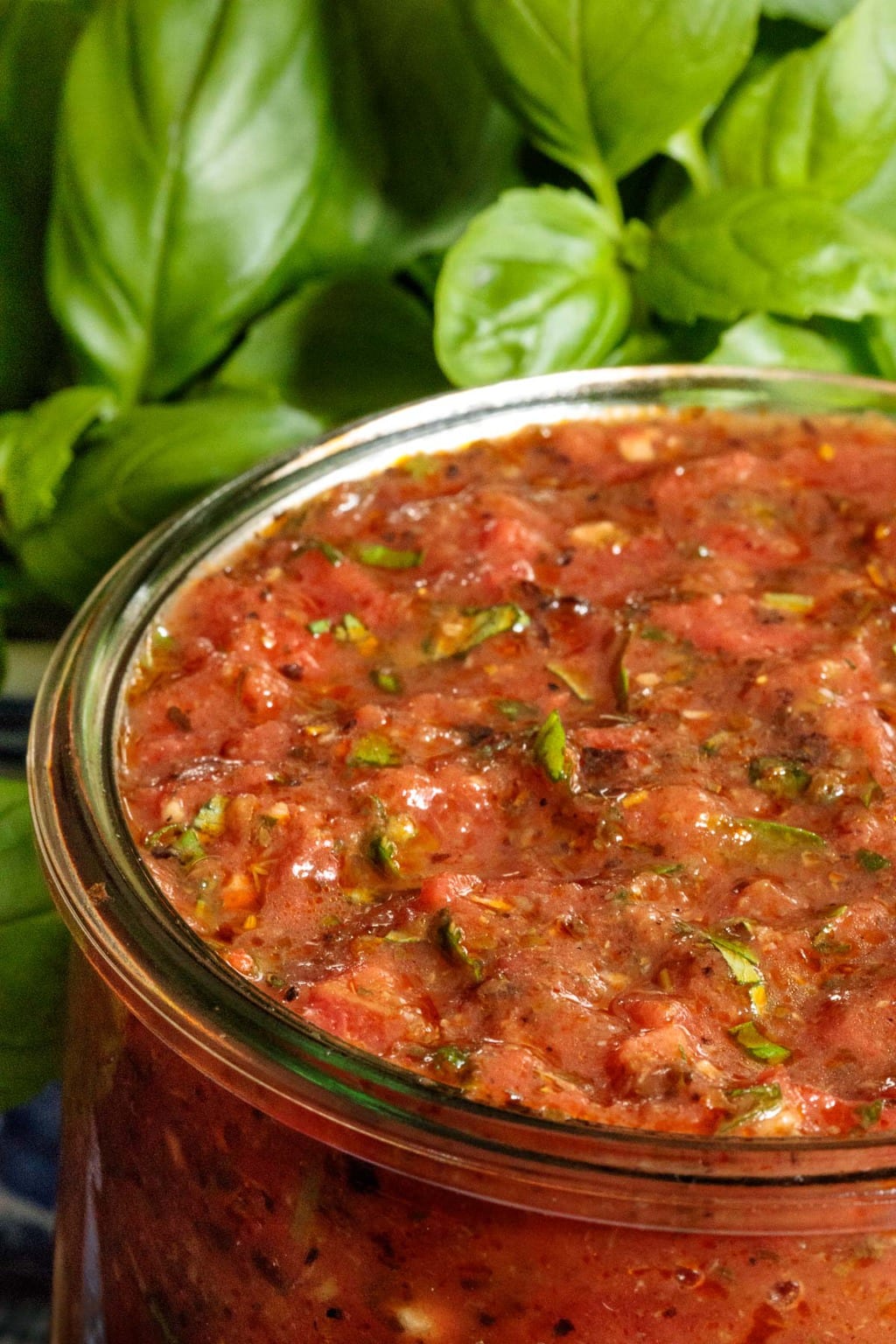 Vertical extreme closeup photo of Quick and Easy Marinara Sauce in a glass Weck jar with fresh basil leaves in the background.