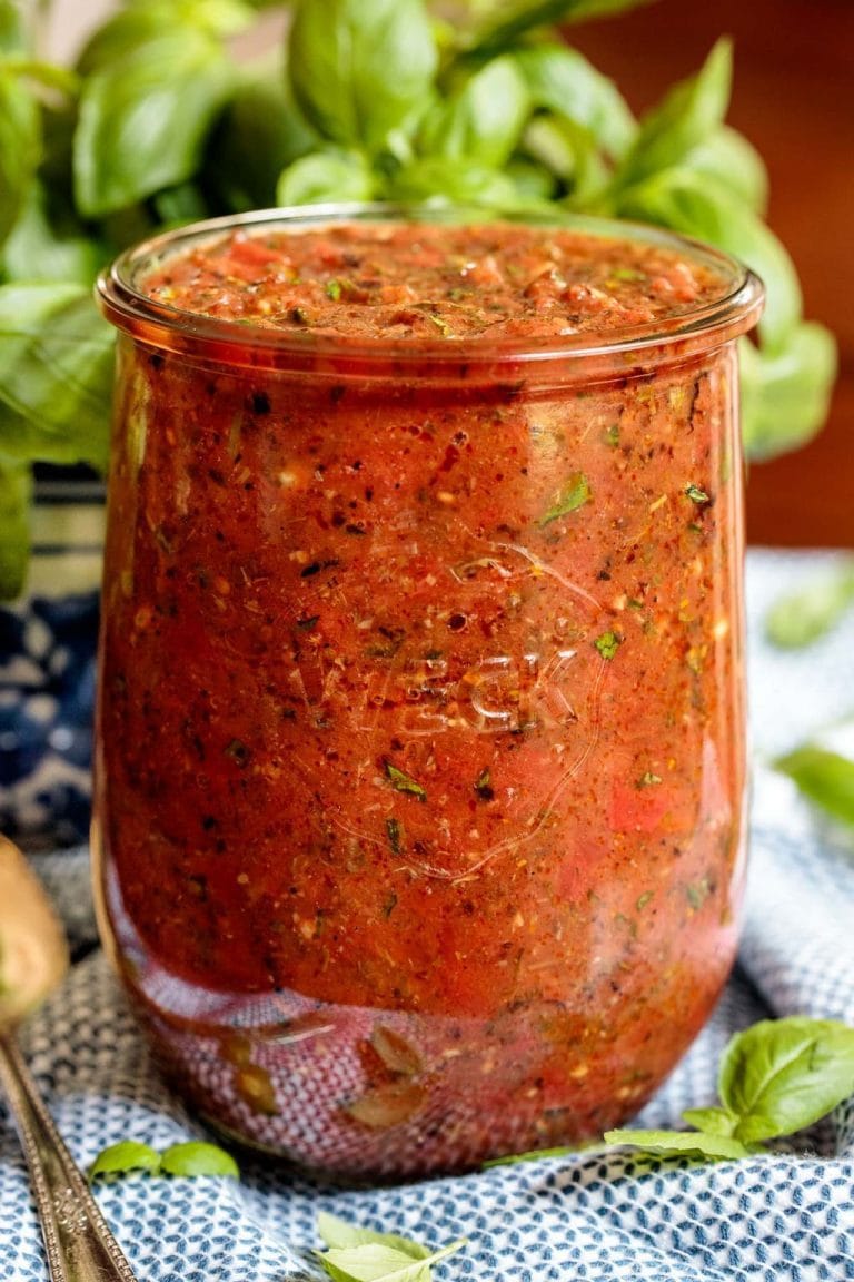 Vertical closeup photo of Quick and Easy Marinara Sauce in a tall glass Weck jar with fresh basil leaves in the background.