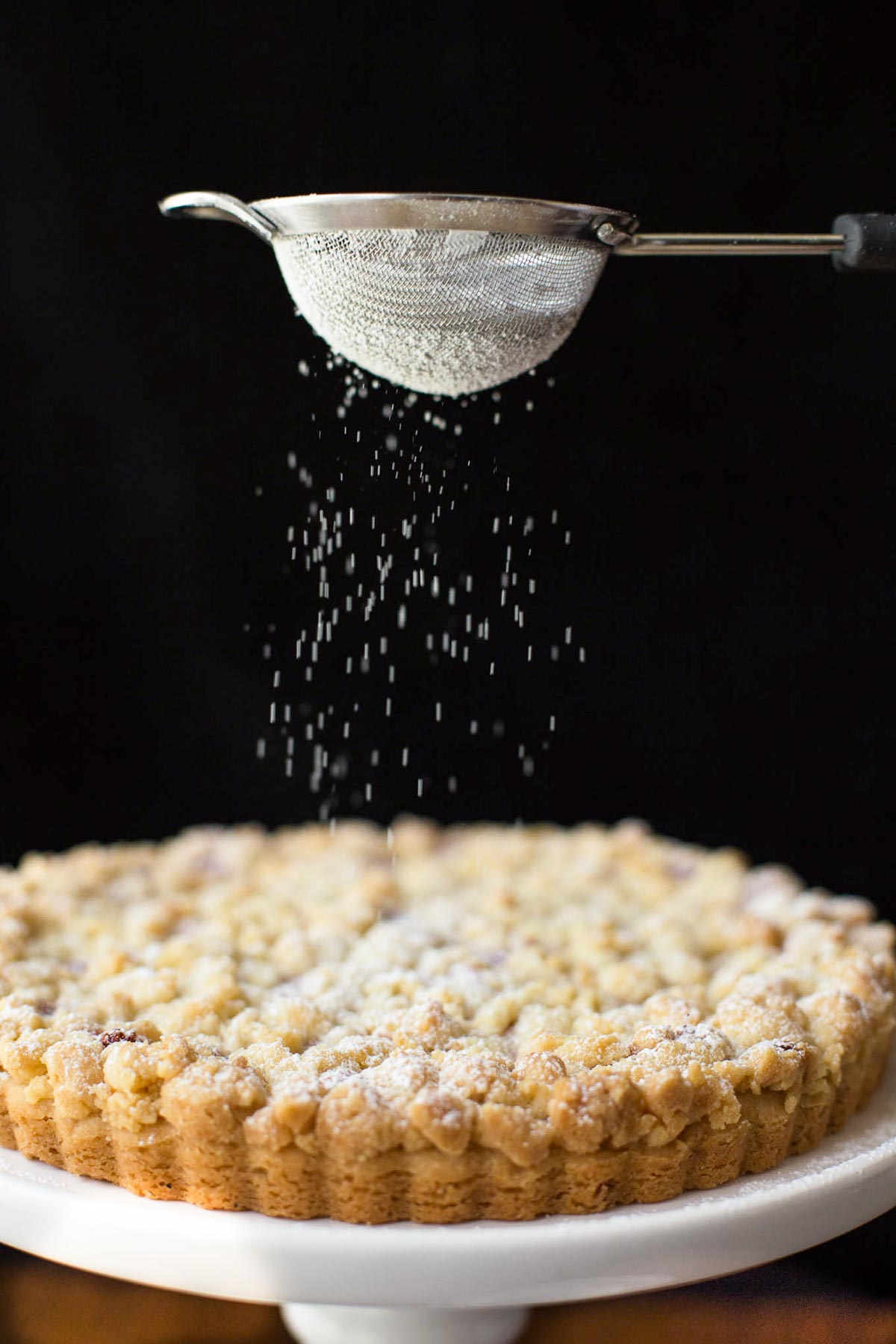 Photo of a Raspberry Jam Shortbread Tart being sprinkled with powdered sugar from a sieve.