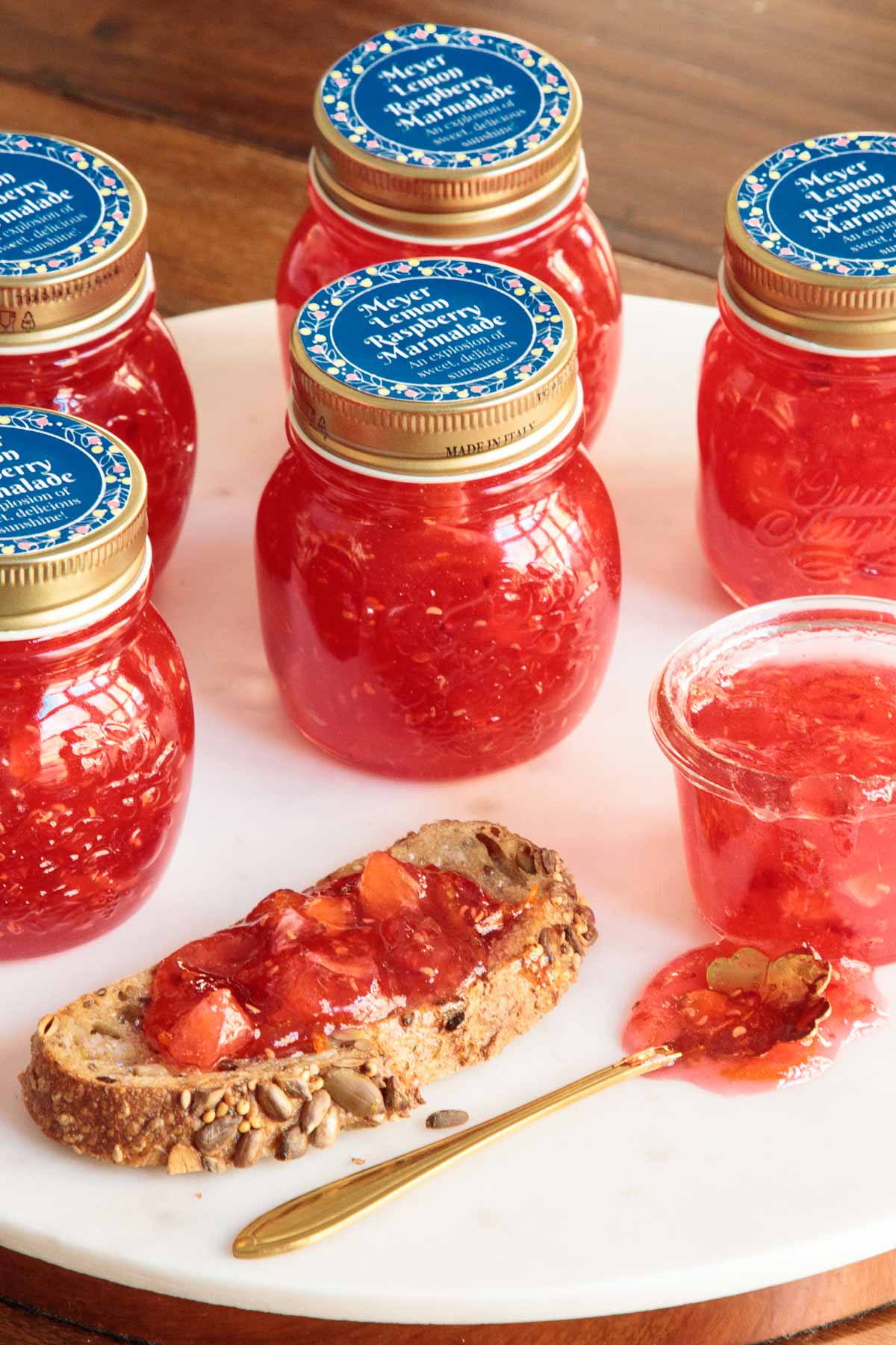 Vertical photo of jars of Raspberry Meyer Lemon Marmalade with blue custom gift labels on the tops of the jars.