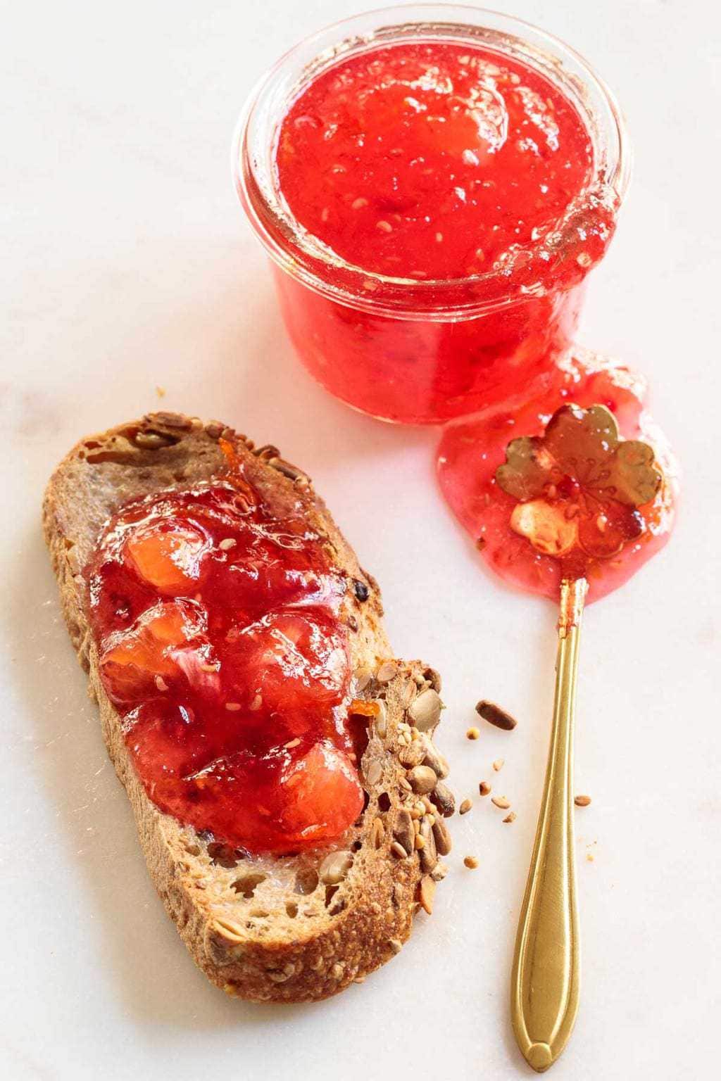 Overhead picture of raspberry meyer lemon marmalade in a glass jar and also spread on toast with a small gold spoon