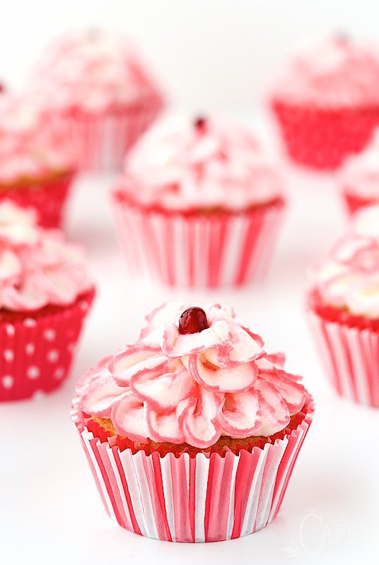 Vertical photo of a batch of Raspberry Pomegranate Swirl Cupcakes in decorative red and white cupcake liners.
