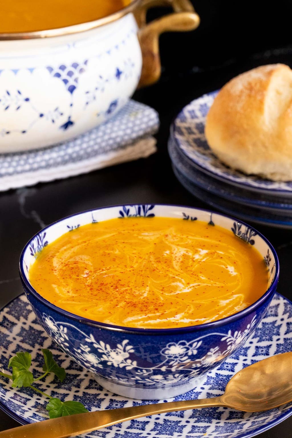 Vertical closeup photo of a bowl of Red Lentil Carrot Ginger Soup in a blue and white patterned serving bowl with a pot of the soup in the background.