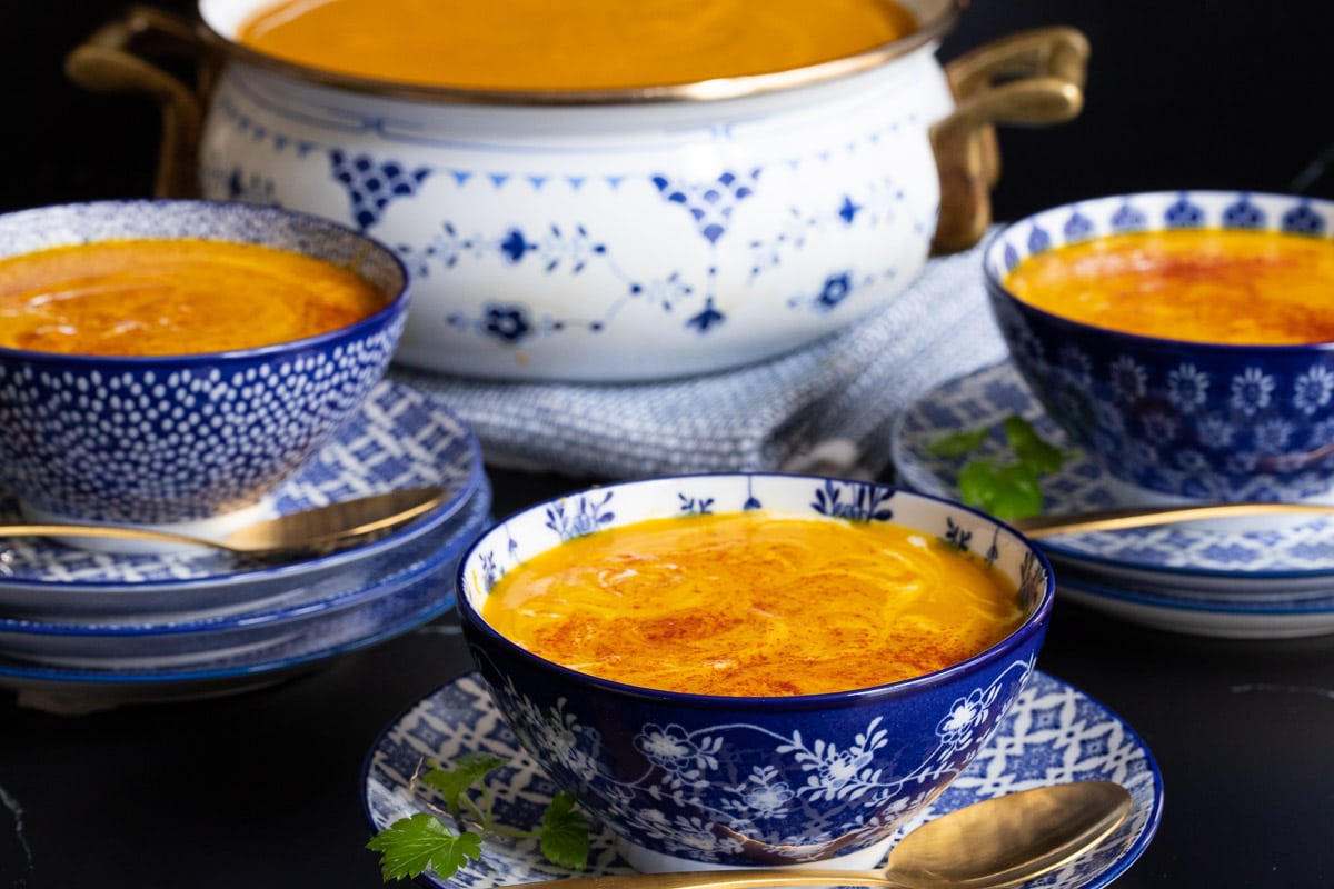 Horizontal photo of blue and white patterned bowls of Gingery Red Lentil Carrot Soup with a soup pot in the background.