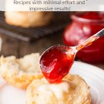 Vertical closeup photo of a buttered Ridiculously Easy Buttermilk Biscuit on a white plate with Strawberry Jam being poured over it.