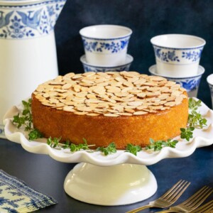 Horizontal photo of a Almond Coconut Cake on a white pedestal cake stand.