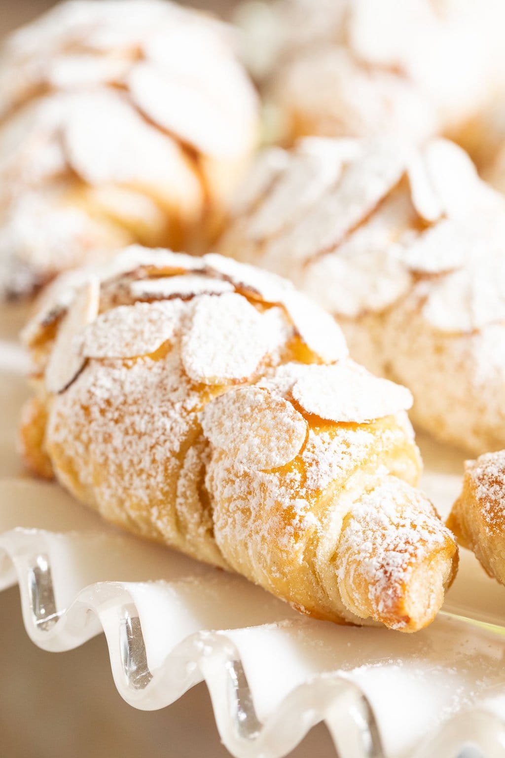 Vertical extreme closeup photo of Easy Almond Croissants on a white glass serving plate.