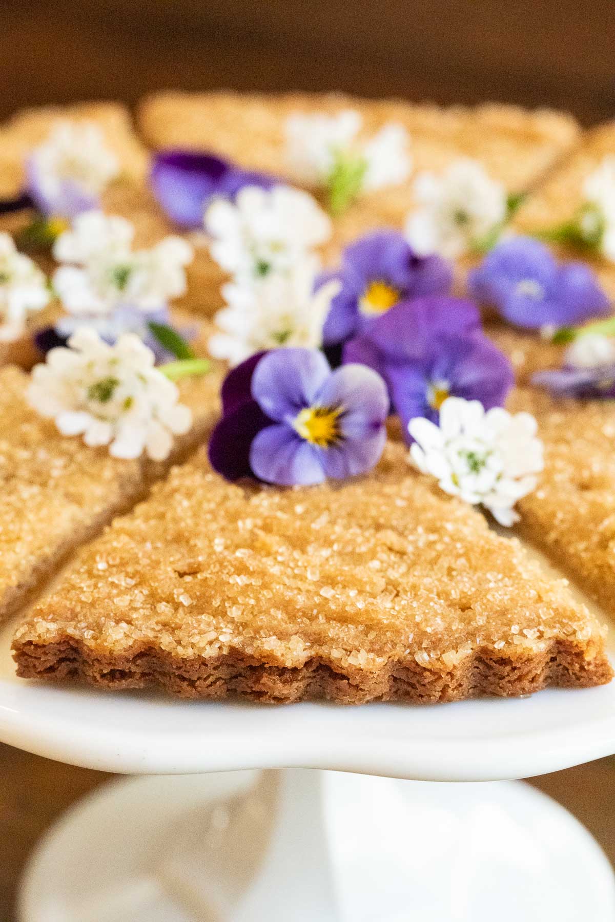 Closeup vertical photo of a slice of Ridiculously Easy Brown Sugar Shortbread on a white pedestal platter.