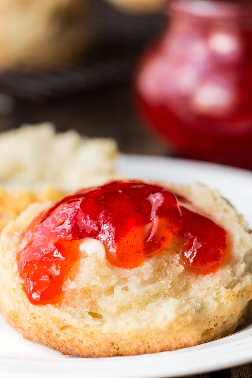 Ultra closeup vertical photo of a Ridiculously Easy Buttermilk Biscuits sliced open with melted butter and strawberry jam on top.