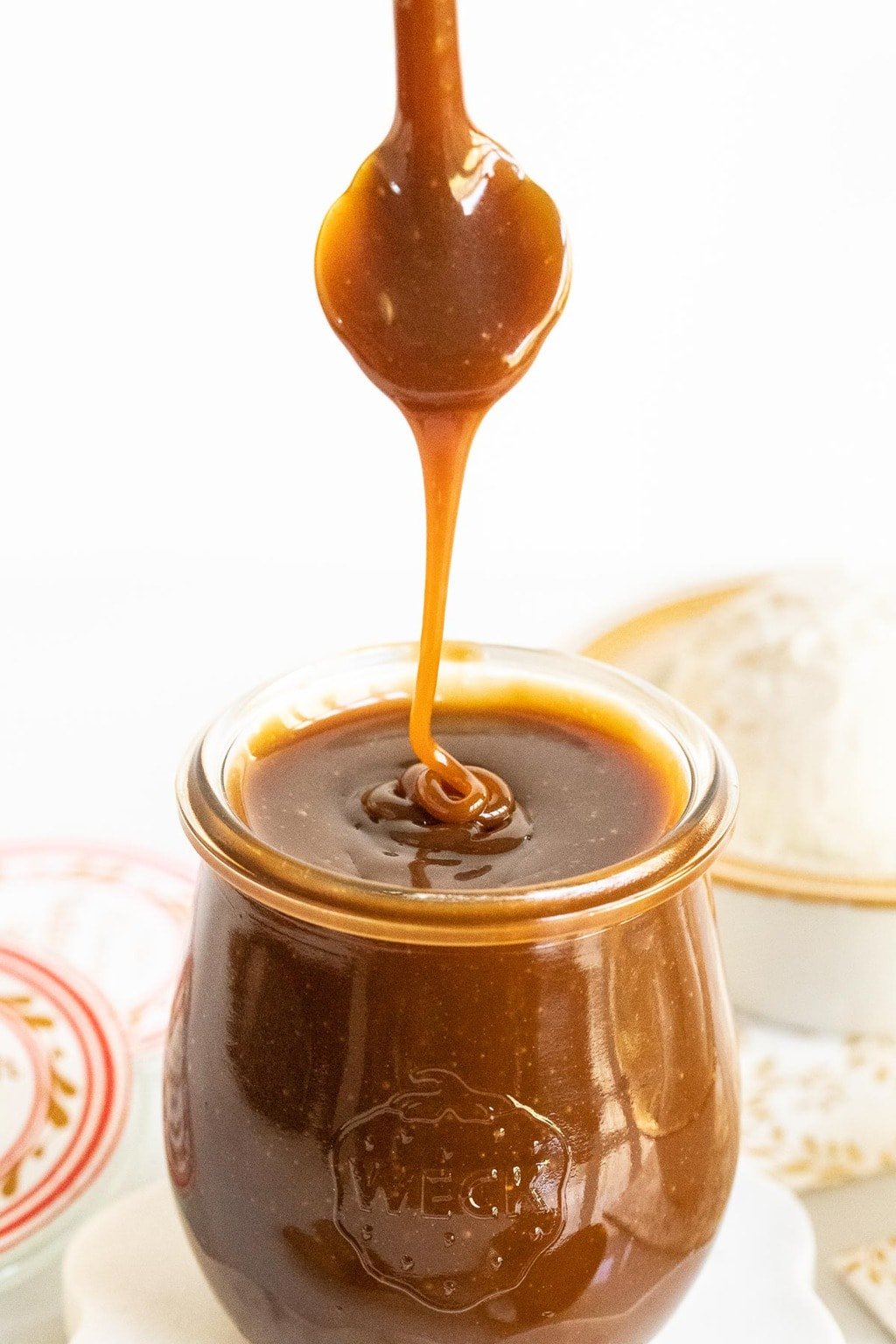 Vertical photo of Ridiculously Easy Butterscotch Sauce in a glass Weck jar with a spoon of the sauce being drizzled back into the jar.
