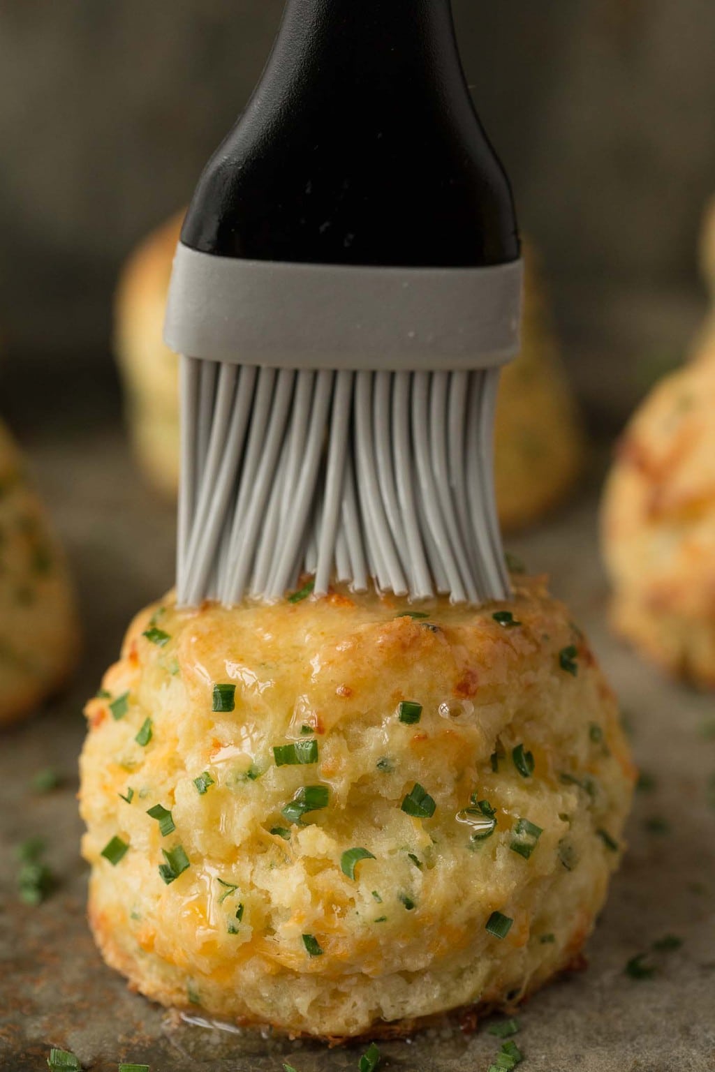 Photo of a basting brush spreading melted butter over Ridiculously Easy Cheddar Chive Biscuits.