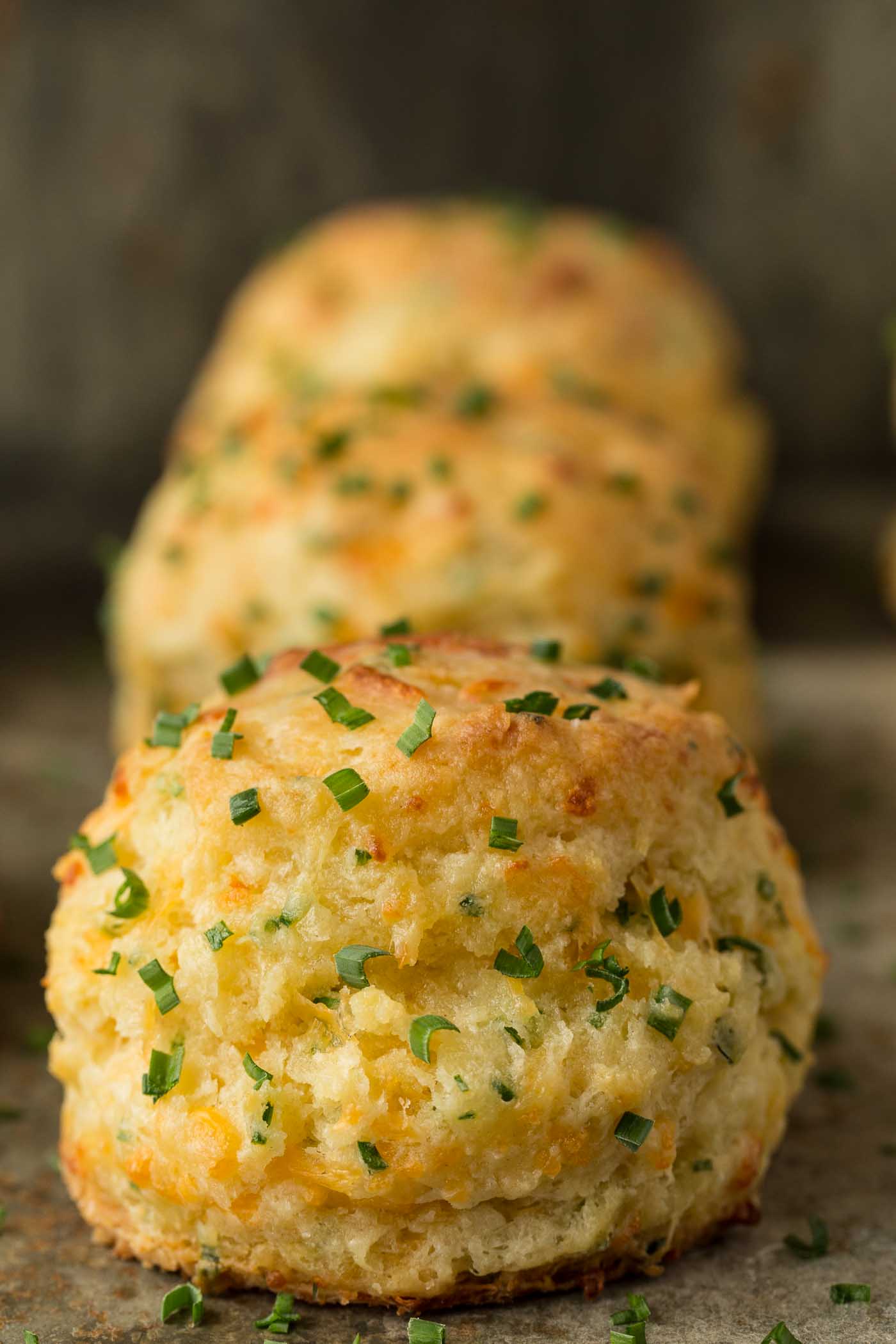 Vertical closeup picture of Ridiculously Easy Cheddar Chive Biscuits lined up behind each other on a slate surface.
