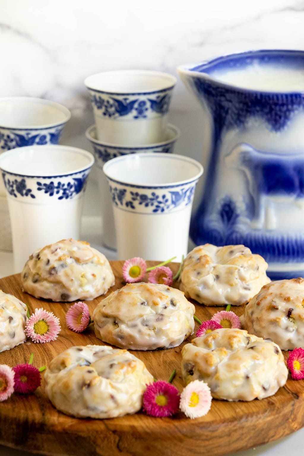 Vertical photo of Ridiculously Easy Chocolate Chip Cherry Scones on a wooden serving board with glasses of milk in blue and white patterned cups in the background.