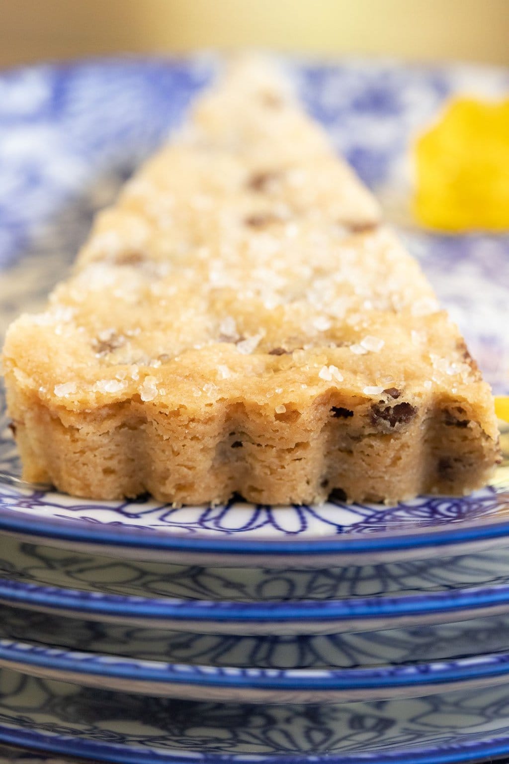 Extreme vertical closeup photo of a wedge of Ridiculously Easy Chocolate Chip Shortbread on a blue and white patterned serving plate.