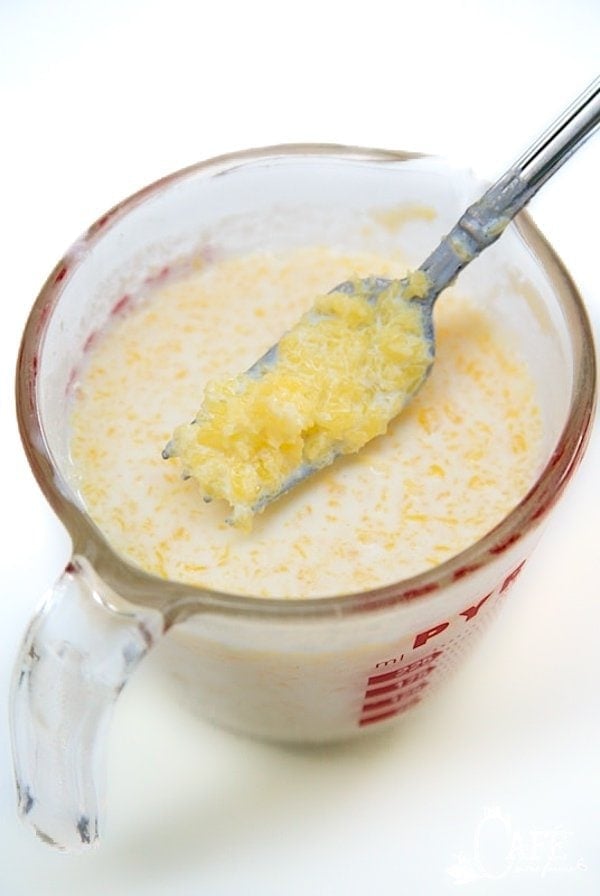 A shot of a Pyrex mixing bowl filled with buttermilk and butter, with a fork holding up globules of the butter above it. 