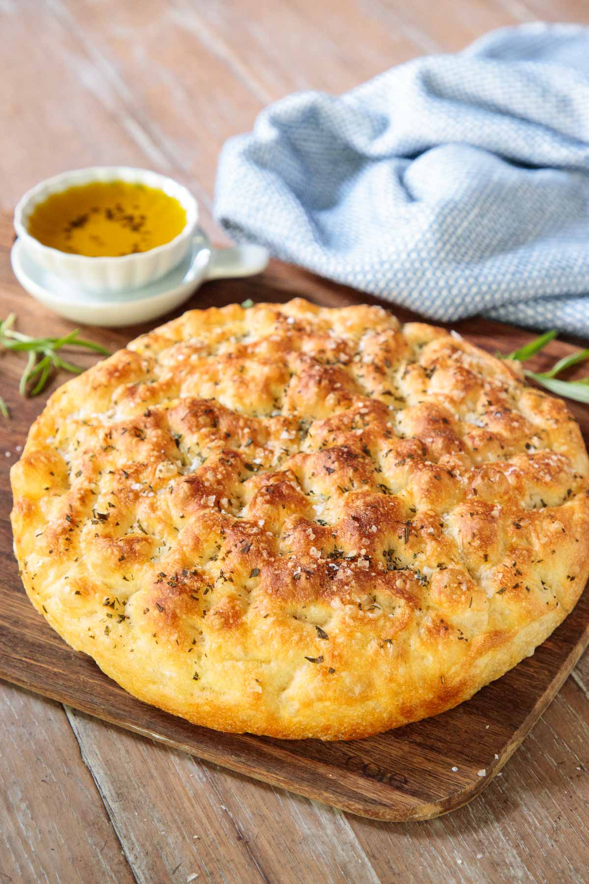 Vertical photo of Ridiculously Easy Focaccia Bread on a wooden cutting board with a small bowl of olive oil.