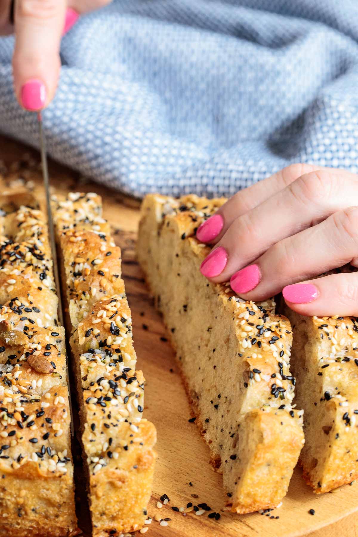 Closeup photo of a person cutting slices of Ridiculously Easy Seeded Focaccia Bread with a bread knife.